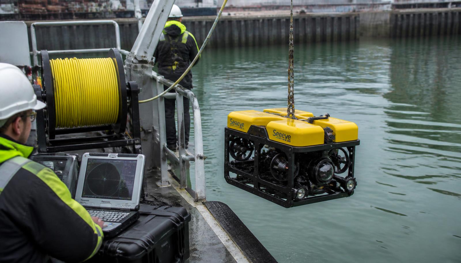 Inspection-class ROV going overboard, with the tether spool and control station on deck.